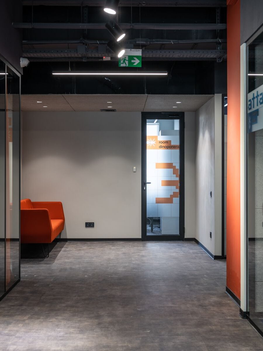 Office corridor with glass partitions and a bright orange lounge sofa