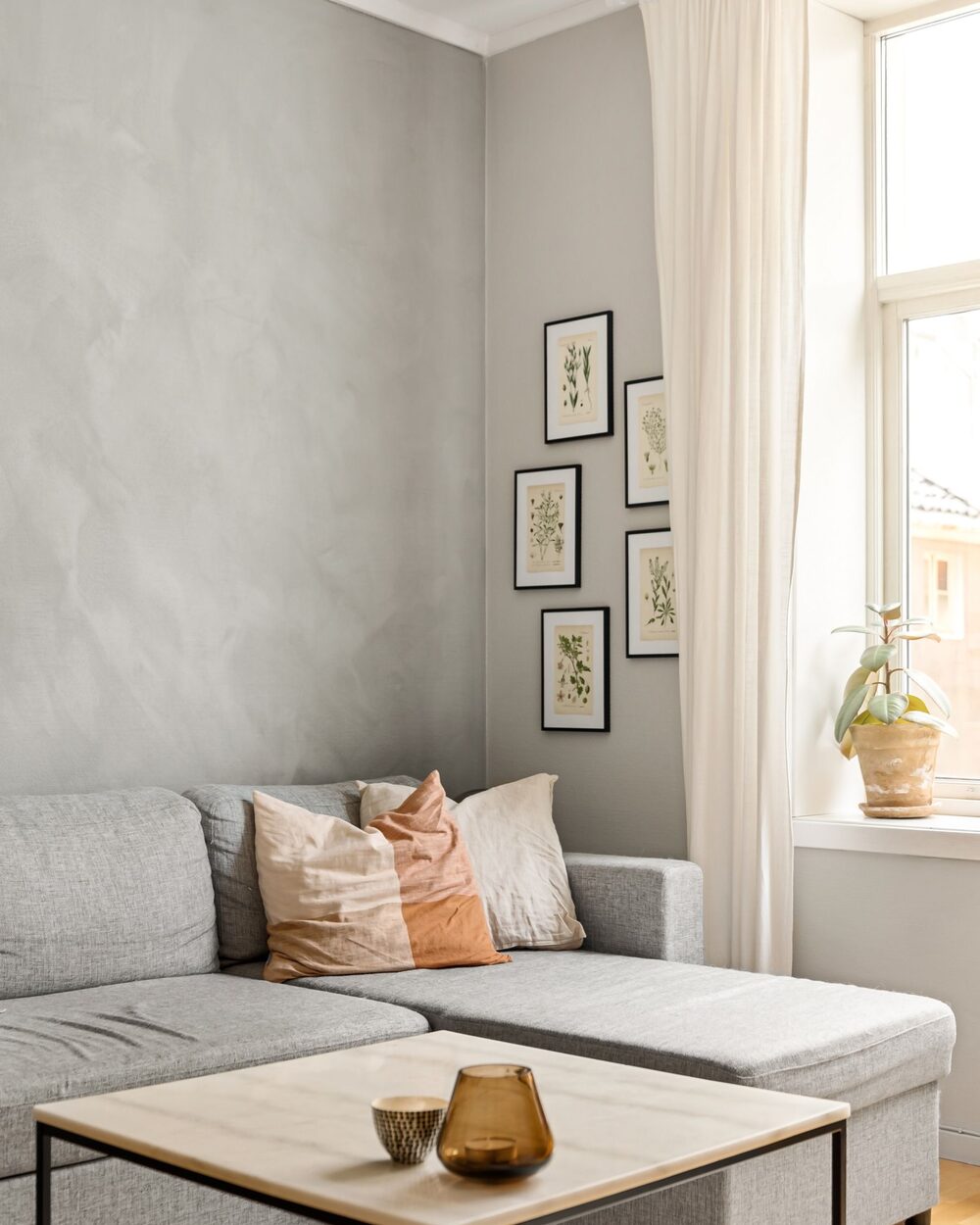 Living room with a grey sofa, framed gallery wall and soft daylight from a tall window